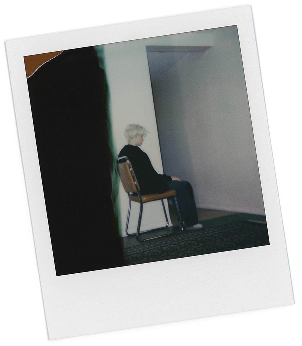Polaroid shot of Tyler sitting on a chair side profile